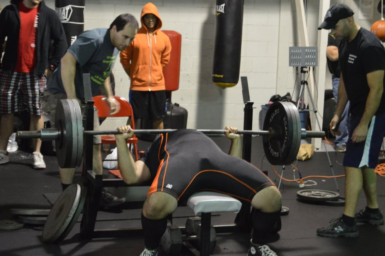 David bench pressing a loaded barbell with spotters in a gym.