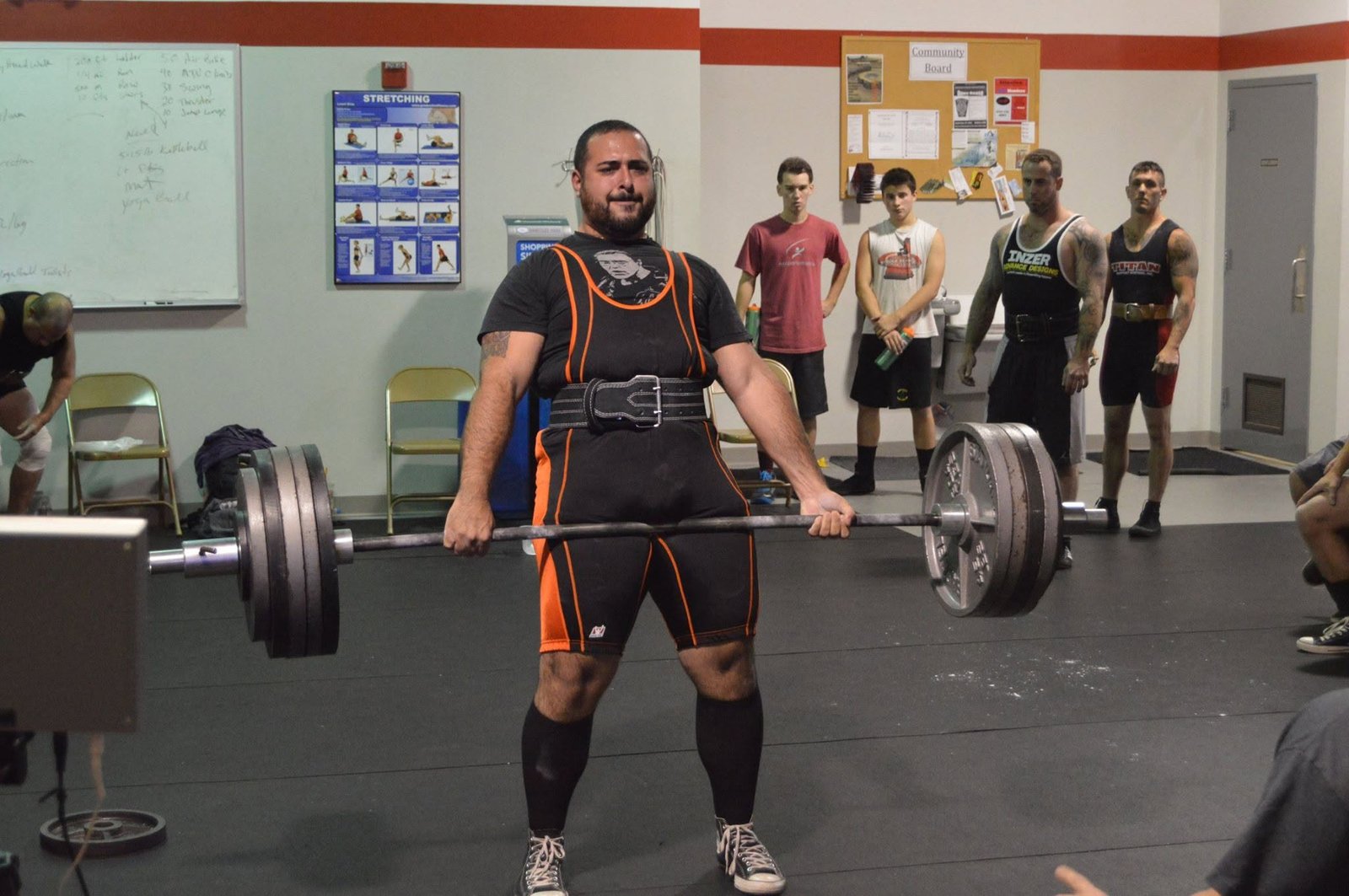 David standing with a loaded barbell at the top of a deadlift.