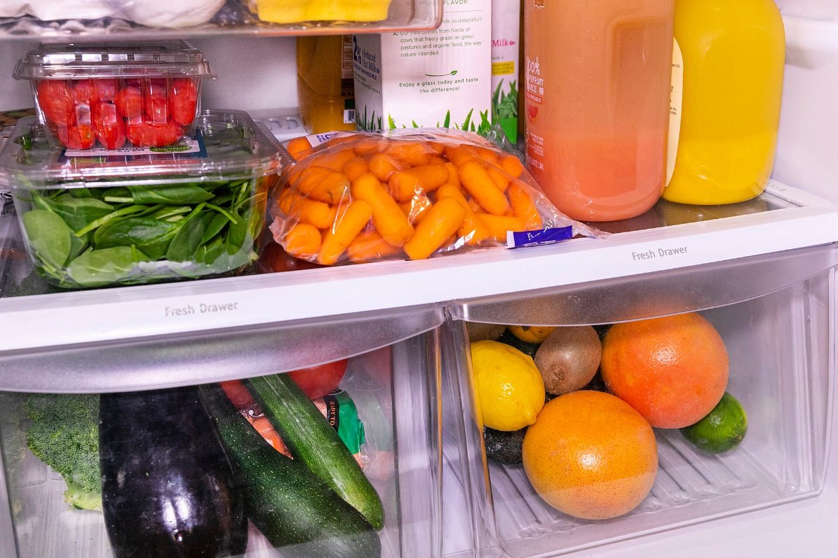 Refrigerator shelves and drawers holding spinach, carrots, citrus fruit, cucumbers and eggplant.
