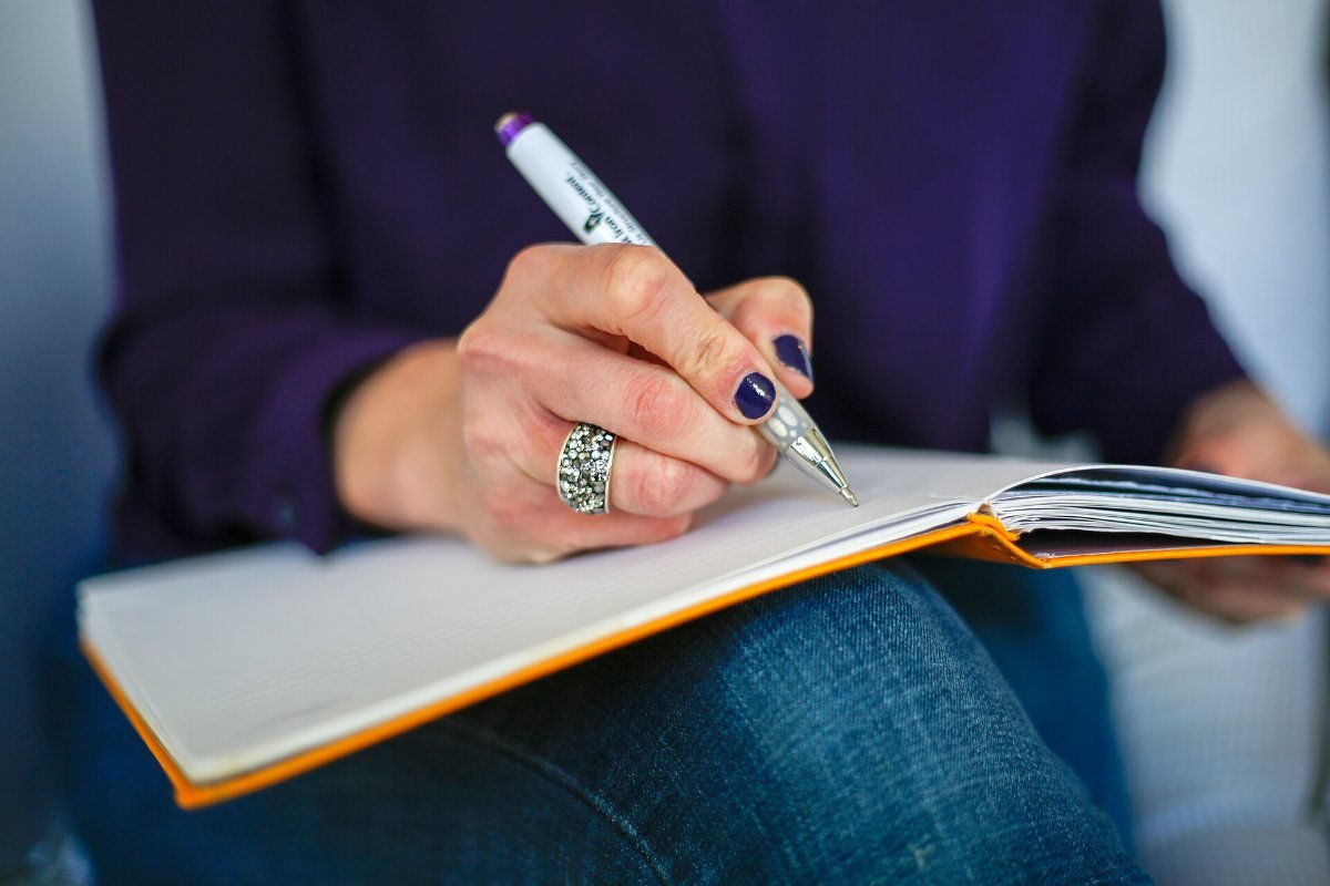 A person writing in an open notebook resting on their lap.