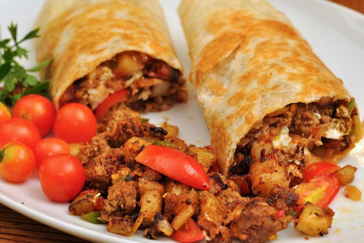Two cut breakfast burritos with tomatoes on a white plate.