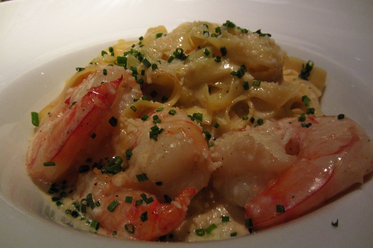 A white bowl of fettuccine in a cream sauce with shrimp and chives.