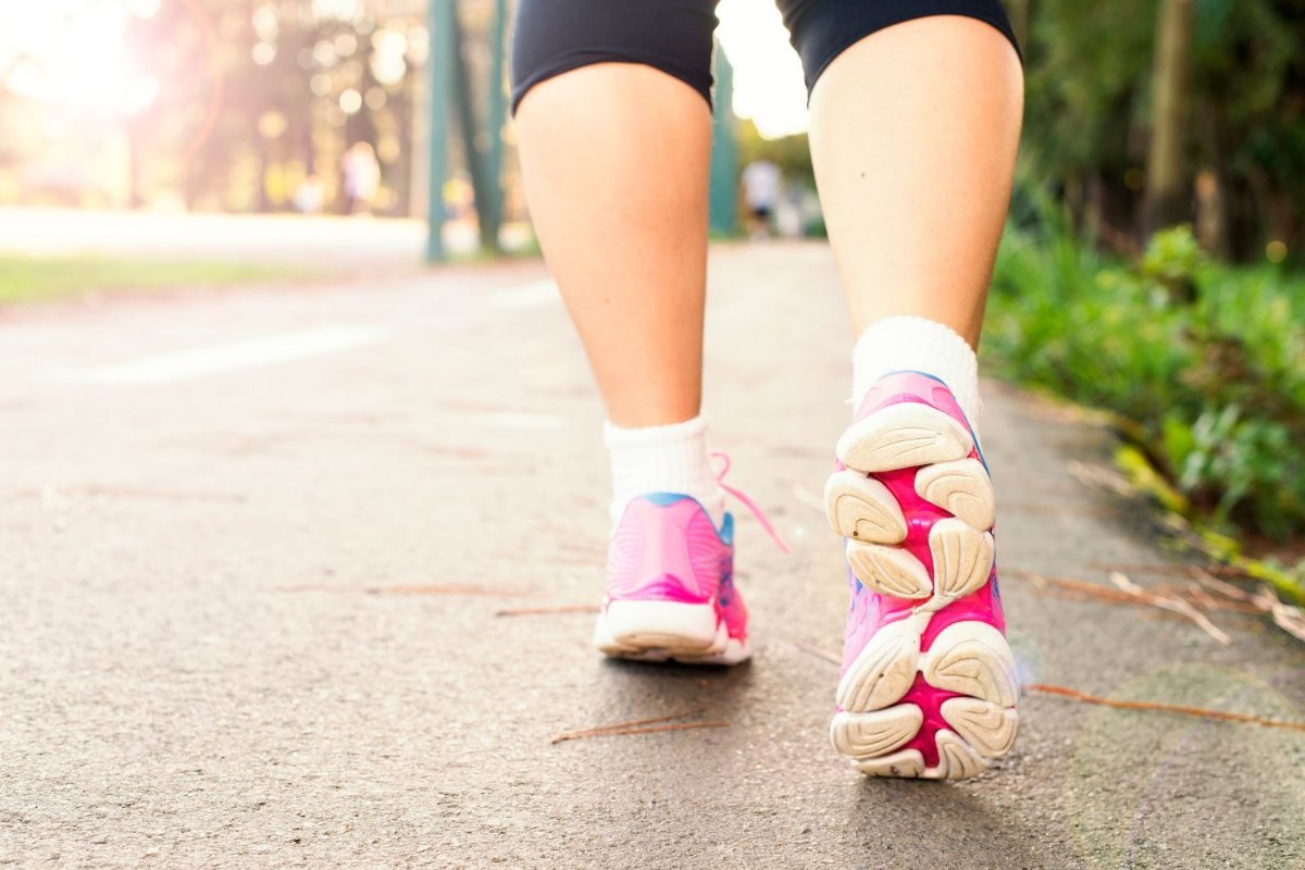 Close-up of a person's legs and pink walking shoes mid-stride on a sunlit path.