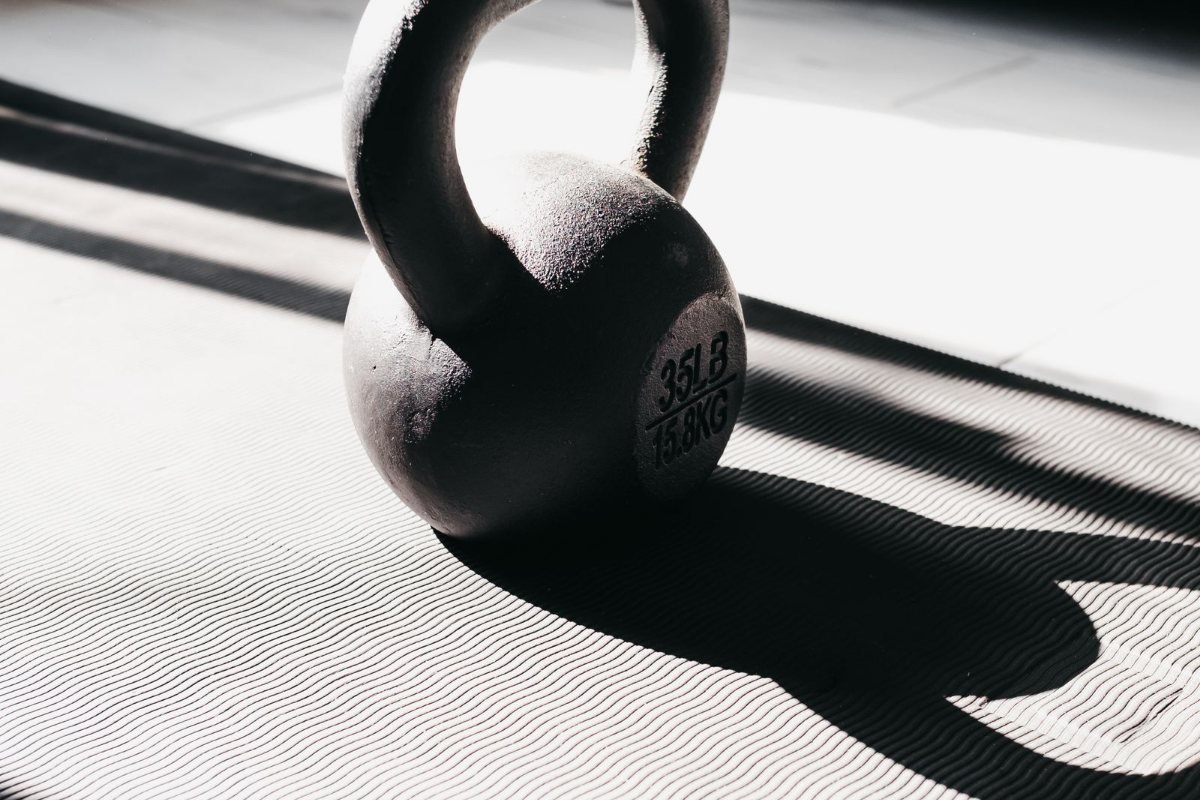 A kettlebell on a mat in strong sunlight, with a long shadow across the floor.