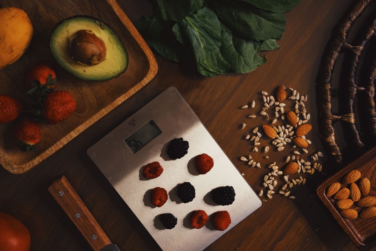 A kitchen scale among avocado, berries and nuts on a wooden board.