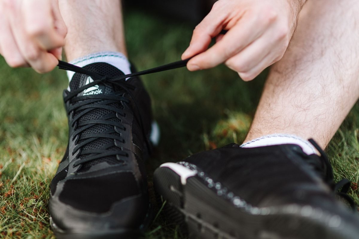 Hands tying a black athletic shoe on grass.