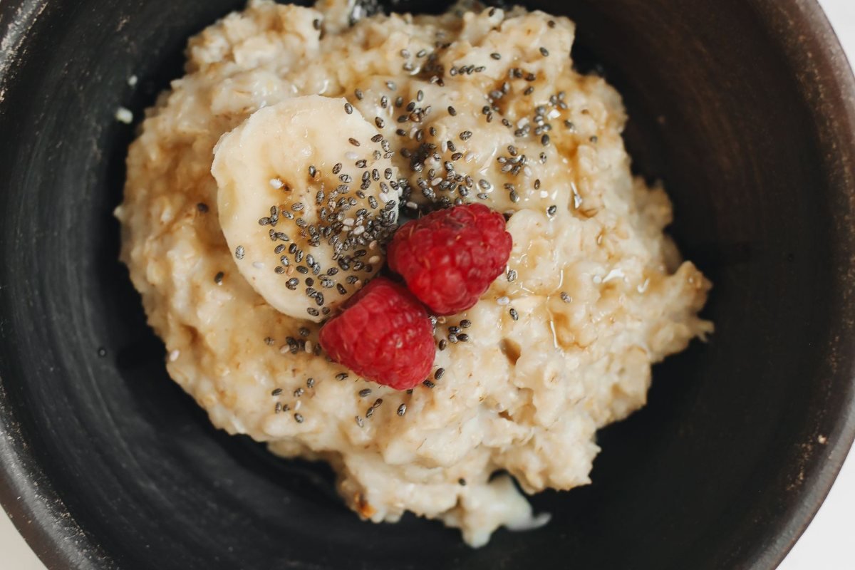 A bowl of oatmeal topped with banana slices, raspberries and chia seeds.