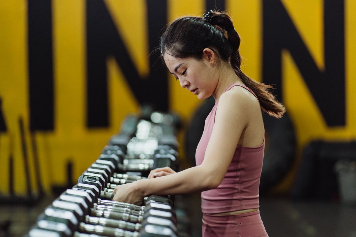 A woman choosing a dumbbell from a gym rack.