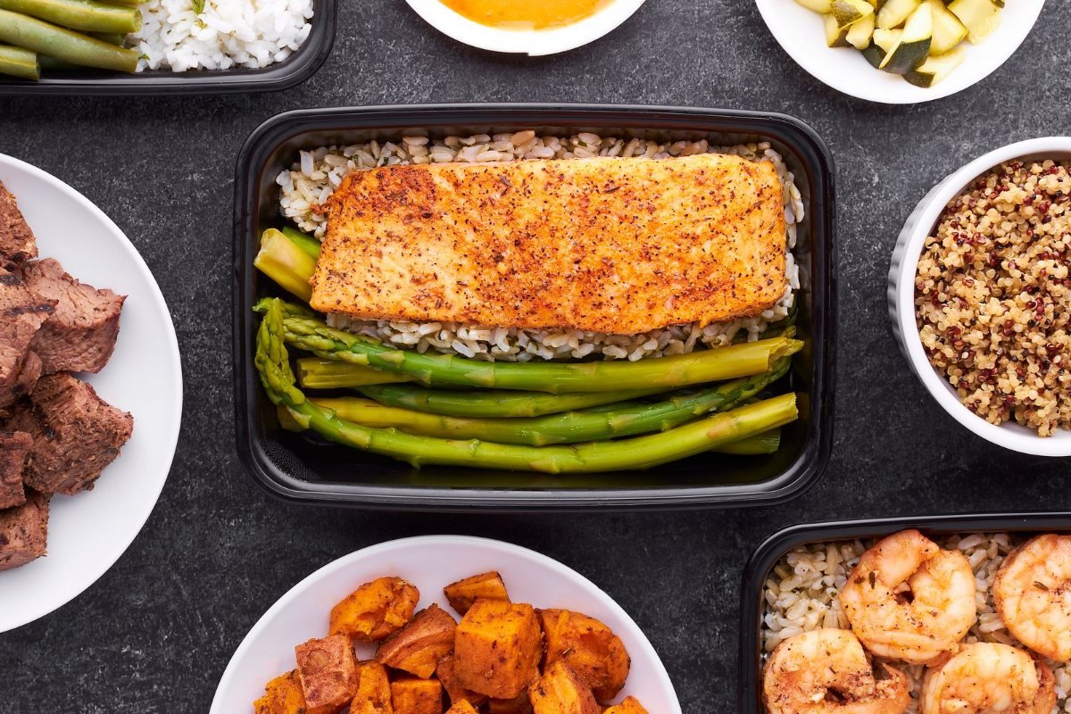 Meal-prep containers with salmon, asparagus, shrimp and sweet potatoes.