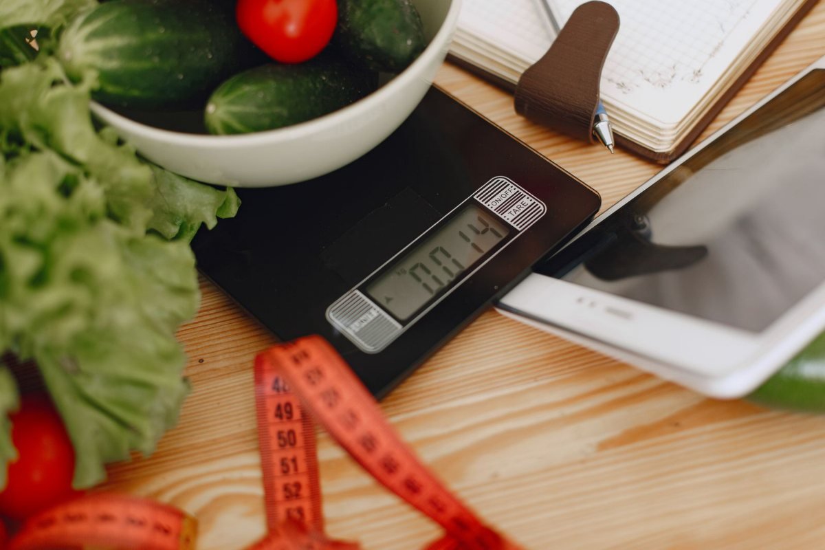 A bowl of vegetables on a kitchen scale with a measuring tape nearby.