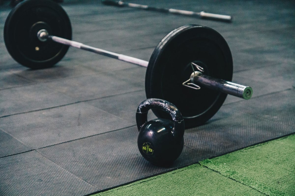 A barbell and a kettlebell on a black gym mat.