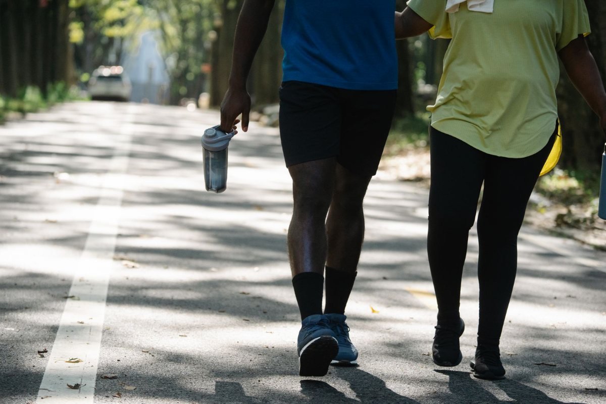 Two people walking side by side down a tree-lined path, one carrying a water bottle.